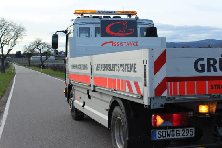 Ein mit Verkehrsmanagementsystemen und Verkehrssicherungsgeräten ausgestatteter LKW steht auf einer Straße, umgeben von Bäumen und Bergen im Hintergrund.