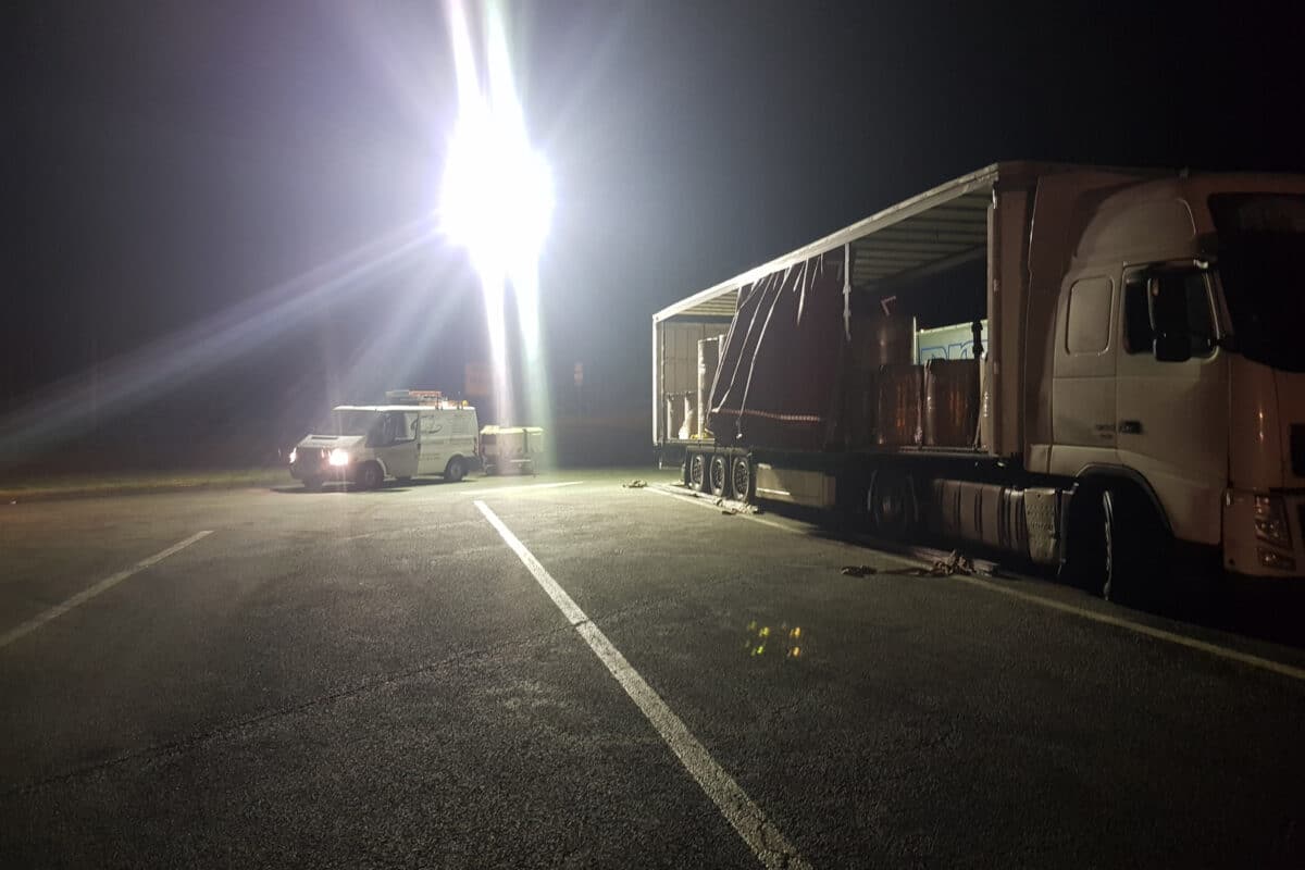 LKW und Transporter parken nachts unter hellem Licht auf einem Gebiet, das wie ein Rastplatz oder Parkplatz aussieht, perfekt für schnelle Abschleppdienste.