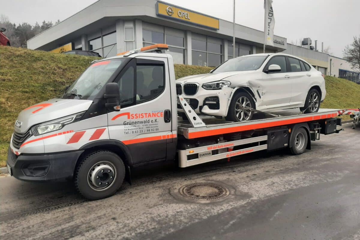 Ein Abschleppwagen des Abschleppdienstes transportiert auf seiner Pritsche einen beschädigten weißen BMW in der Nähe eines Autohauses.
